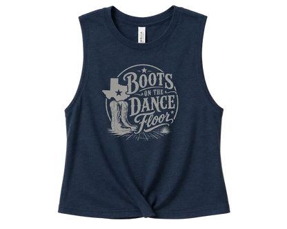 A sleeveless navy blue crop top with a distressed light gray graphic on the front that reads 'Boots on the Dance Floor' with cowboy boots and a Texas-shaped boot outline, shown on a solid beige background.